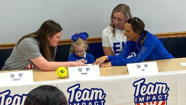 Reese signs her name as EIU softball players and coaches look on