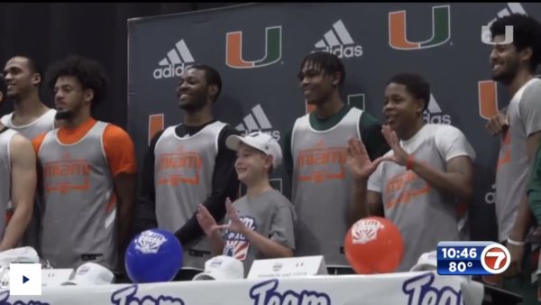 University of Miami basketball players pose for a photo alongside their super fan